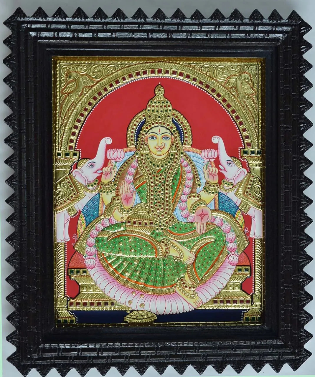 Decorative artwork of a deity with intricate details in a black frameGaja Lakshmi in Tanjore 