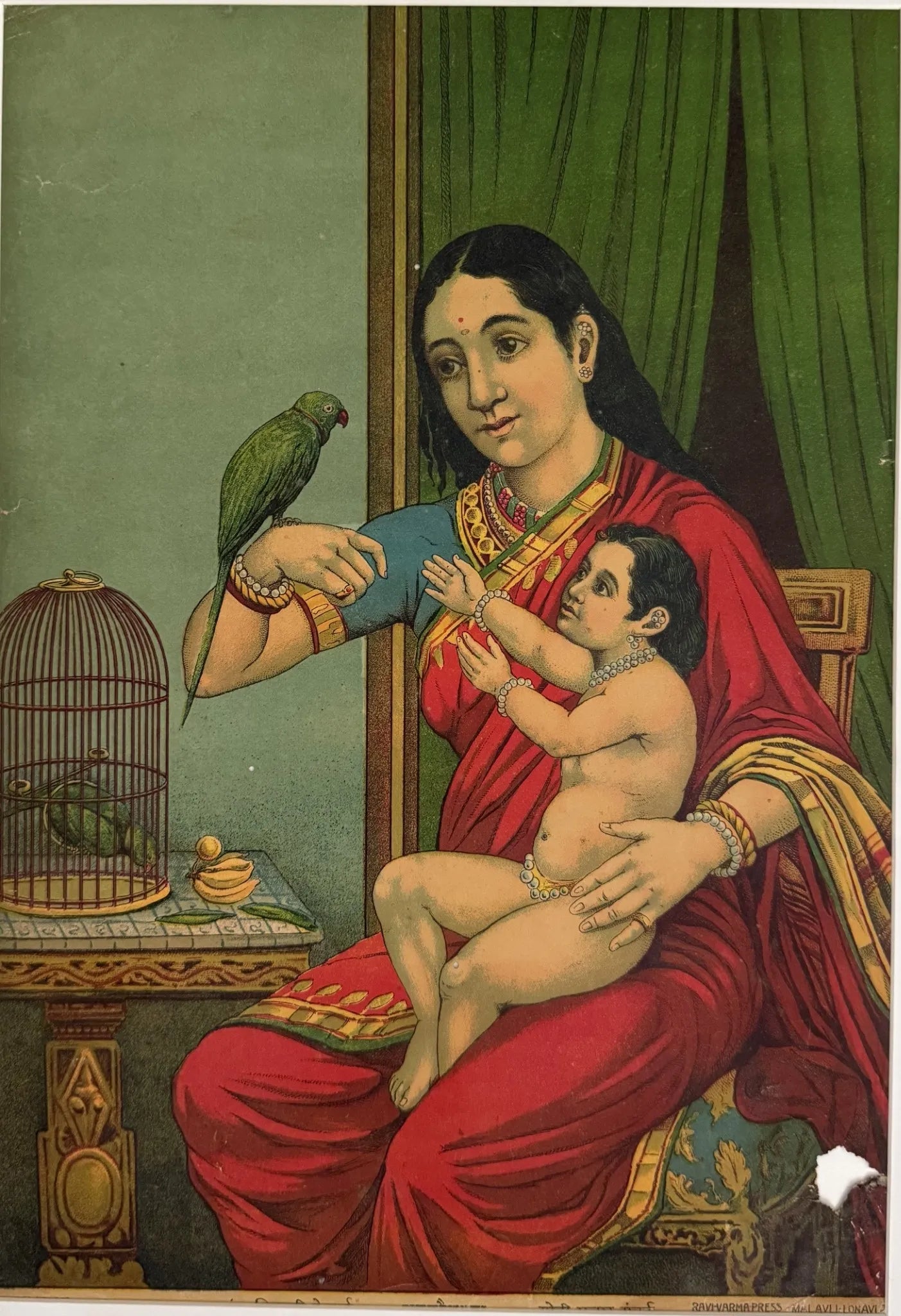 Woman in a red sari holding a child with a parrot on her arm, sitting next to a green curtain. Raja Ravi Varma Oleograph 